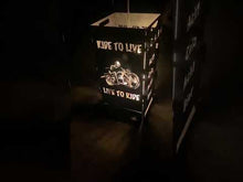 Laden und Abspielen von Videos im Galerie-Viewer, Brennende Metallkiste mit kunstvollen Auschnitten, die ein Biker-Motorrad darstellen, in einem dramatischen Lichtspiel.